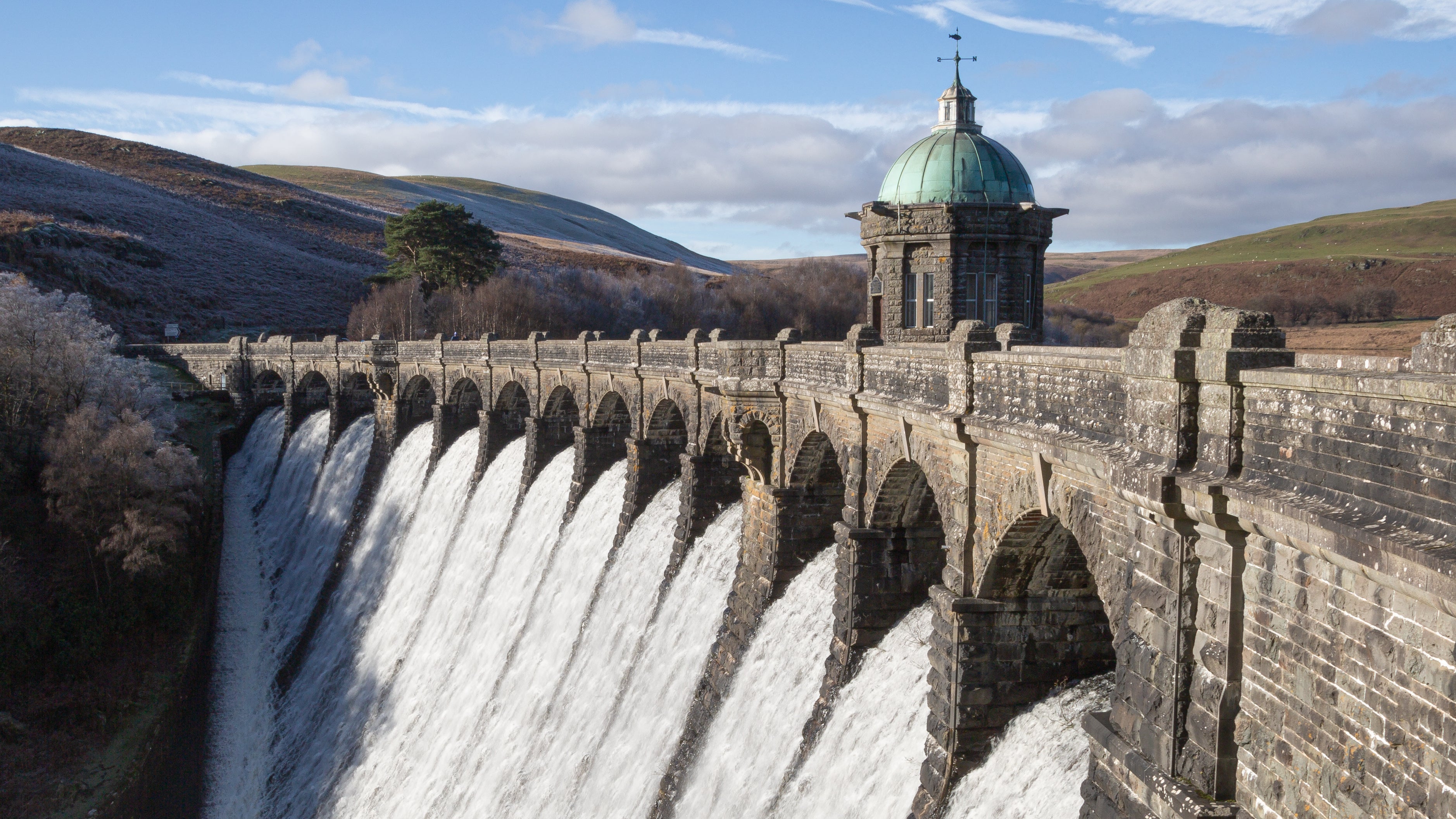 Large dam with water flowing over it, under a clear blue sky.